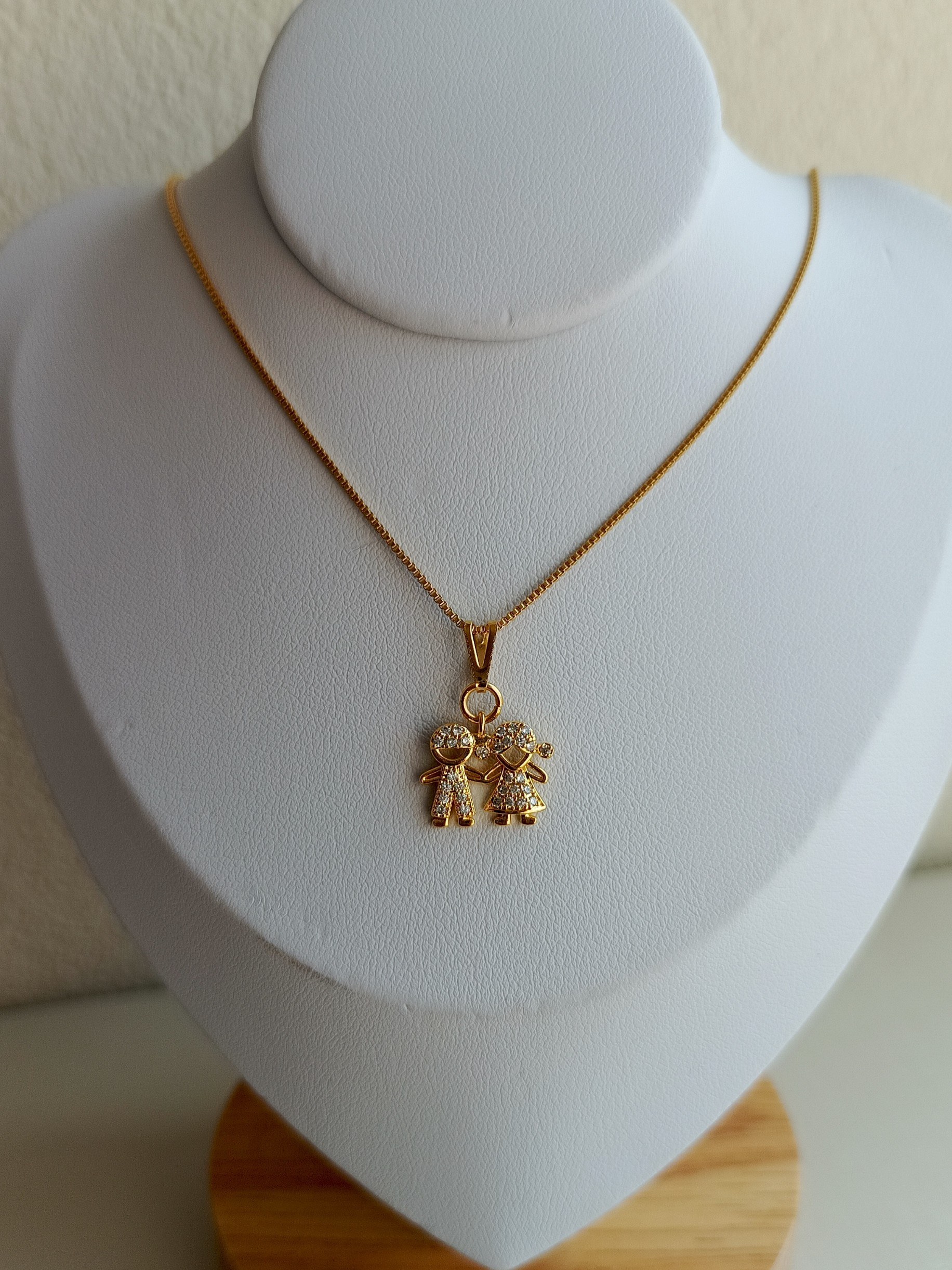 Colar dourado com pingente de duas crianças